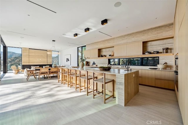 kitchen with a center island with sink, light brown cabinets, plenty of natural light, pendant lighting, and oven