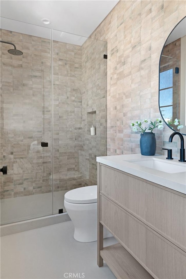 bathroom featuring tile walls, vanity, a shower with door, and toilet