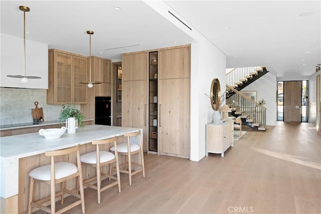 kitchen featuring a kitchen bar, black appliances, hanging light fixtures, and light wood-type flooring