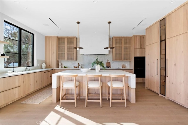 kitchen featuring a kitchen island, tasteful backsplash, a kitchen bar, light brown cabinetry, and light wood-type flooring