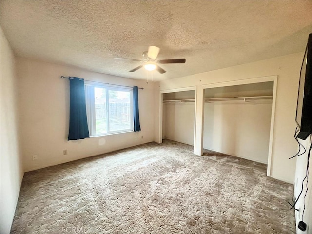 unfurnished bedroom featuring ceiling fan, two closets, carpet floors, and a textured ceiling