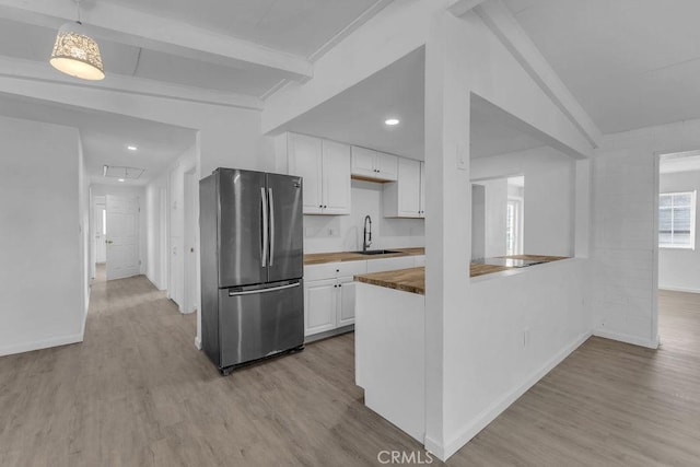 kitchen with white cabinets, wood counters, pendant lighting, stainless steel refrigerator, and sink