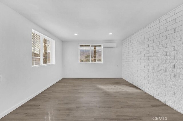 unfurnished room featuring dark wood-type flooring, brick wall, and a wall unit AC