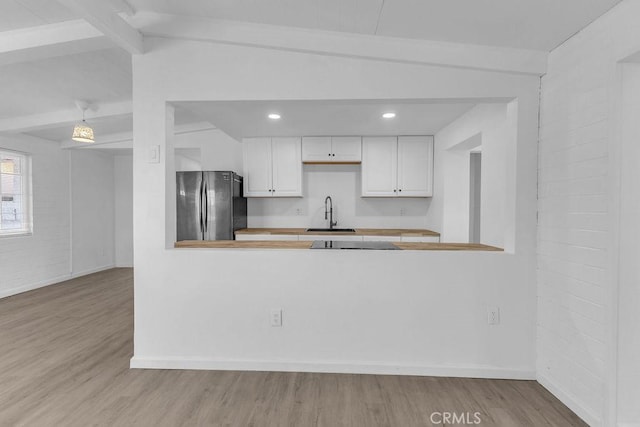 kitchen featuring kitchen peninsula, stainless steel refrigerator, light hardwood / wood-style floors, lofted ceiling with beams, and white cabinets