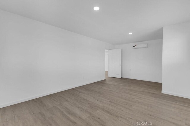 empty room with an AC wall unit and light wood-type flooring