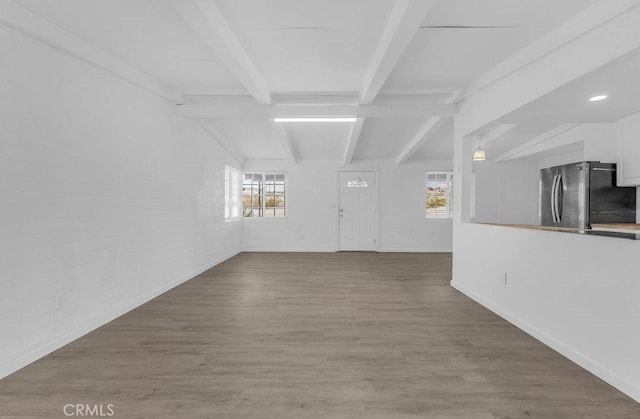 unfurnished living room with hardwood / wood-style flooring, brick wall, and vaulted ceiling with beams