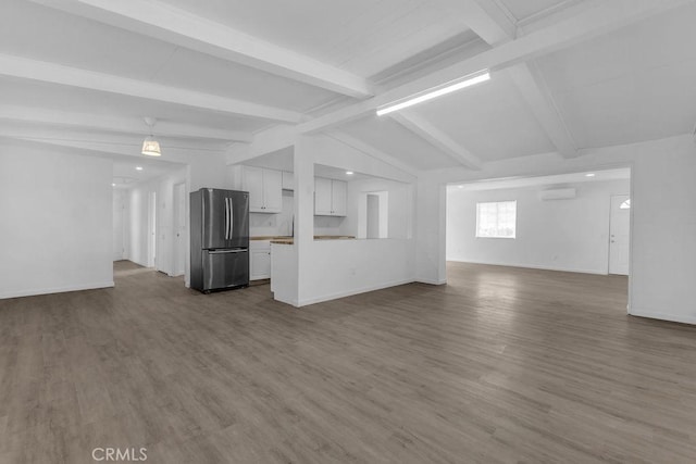 unfurnished living room featuring a wall unit AC, vaulted ceiling with beams, and hardwood / wood-style floors