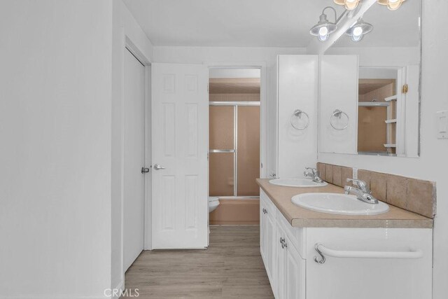 full bathroom featuring toilet, vanity, hardwood / wood-style floors, and bath / shower combo with glass door