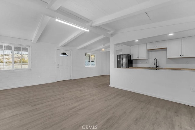 kitchen with light wood-type flooring, sink, vaulted ceiling with beams, white cabinets, and black fridge