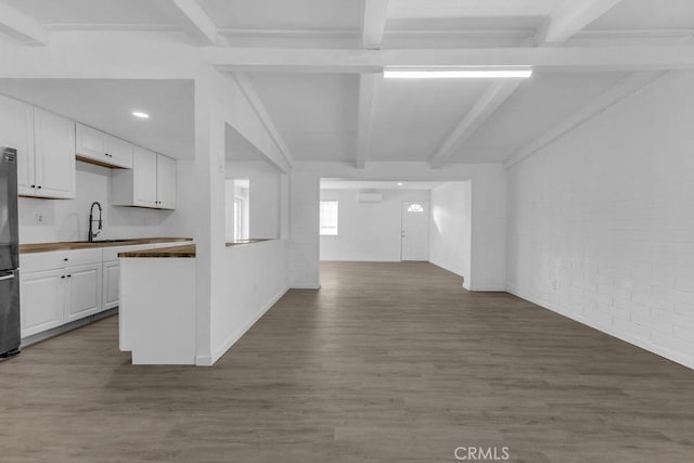 kitchen with vaulted ceiling with beams, wood-type flooring, stainless steel fridge, sink, and white cabinetry