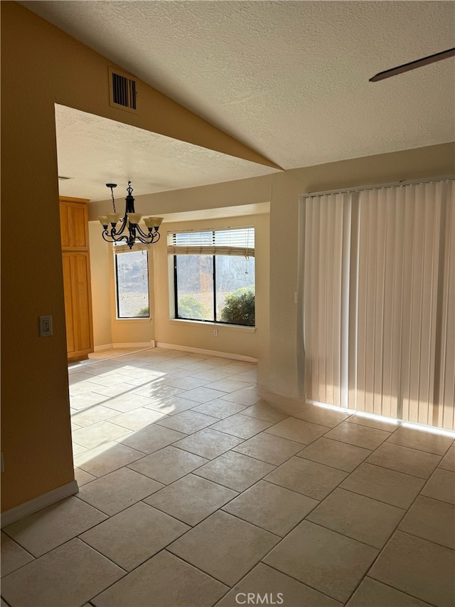 unfurnished room featuring a textured ceiling, vaulted ceiling, a chandelier, and light tile patterned flooring