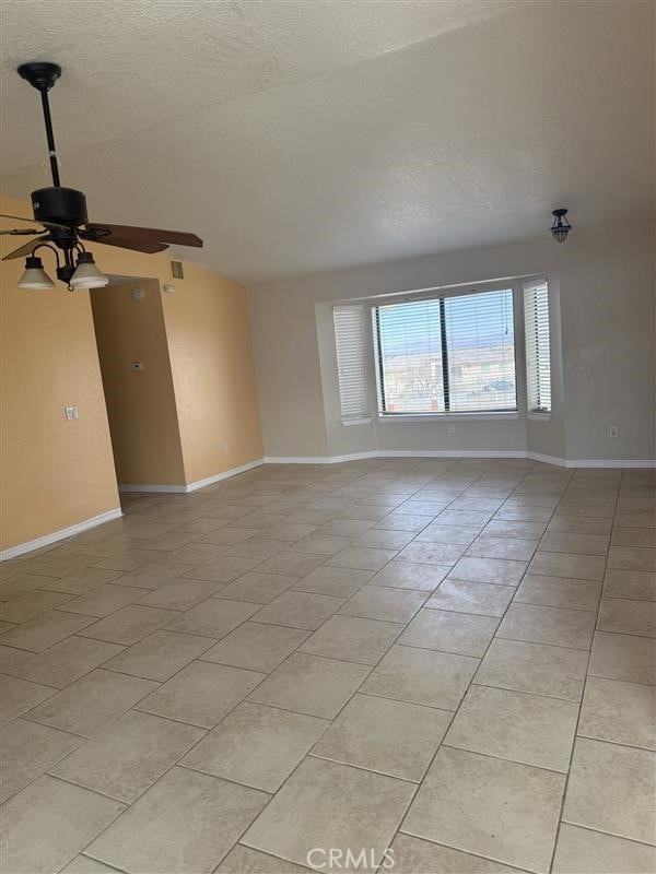 spare room featuring light tile patterned floors, a textured ceiling, a ceiling fan, and baseboards