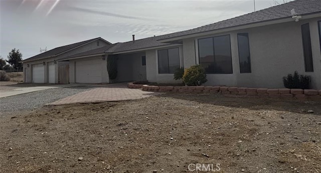 ranch-style home with a garage, driveway, a shingled roof, and stucco siding