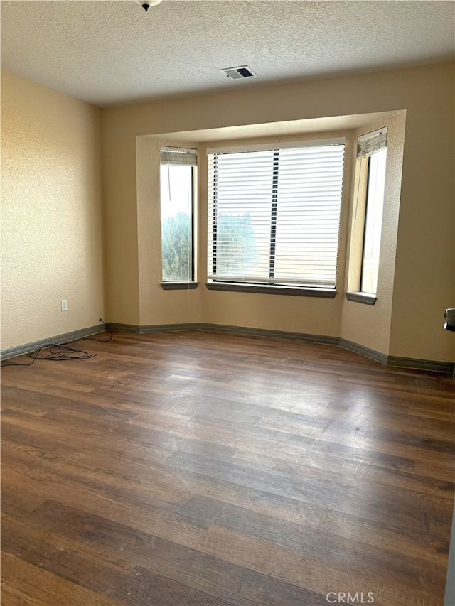 spare room featuring baseboards, visible vents, dark wood finished floors, a textured wall, and a textured ceiling