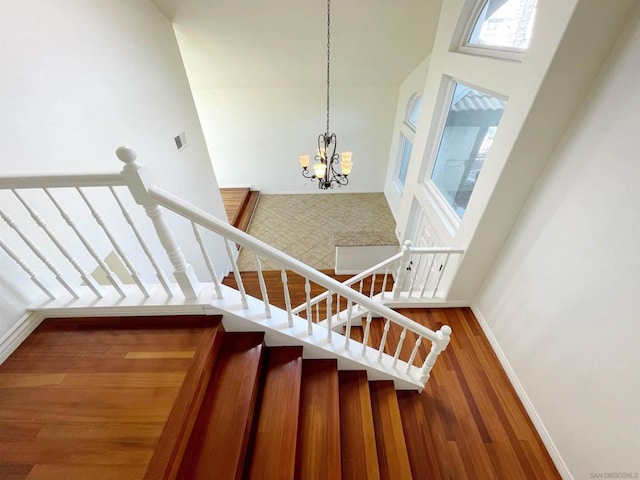 staircase with a towering ceiling, hardwood / wood-style floors, and an inviting chandelier