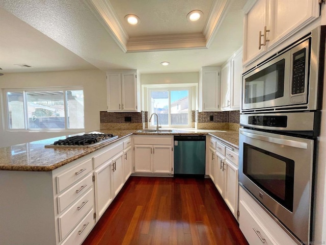 kitchen featuring appliances with stainless steel finishes, white cabinetry, decorative backsplash, a raised ceiling, and light stone countertops