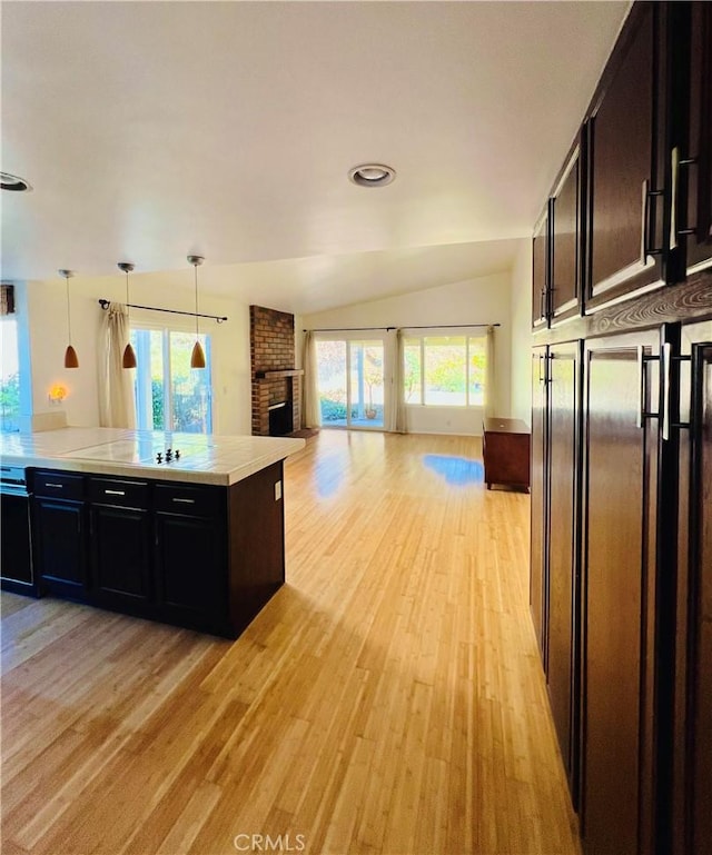 kitchen with pendant lighting, lofted ceiling, light hardwood / wood-style floors, light stone countertops, and a brick fireplace