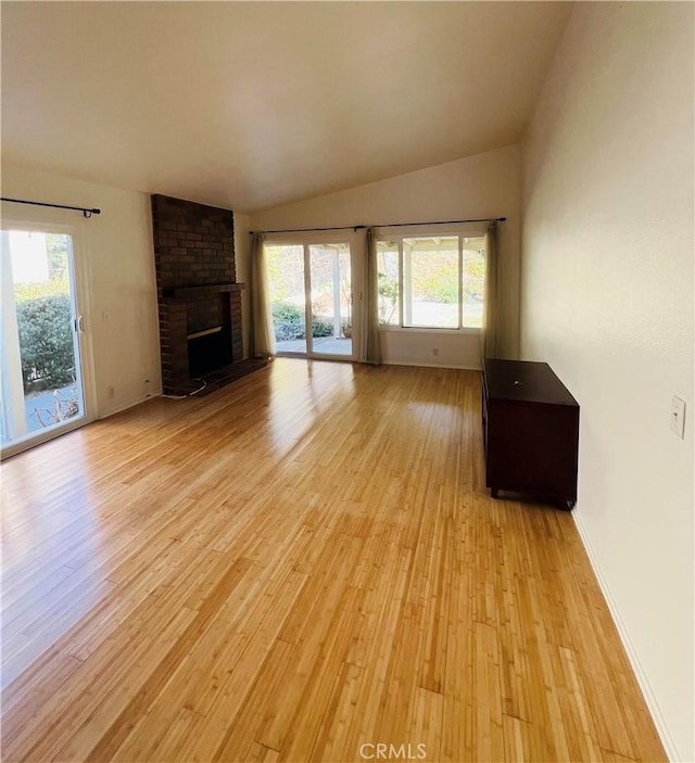 unfurnished living room featuring a brick fireplace, lofted ceiling, plenty of natural light, and light hardwood / wood-style flooring