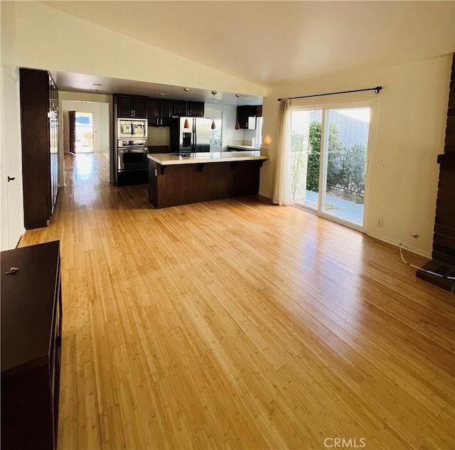 kitchen with vaulted ceiling, stainless steel appliances, kitchen peninsula, and light wood-type flooring