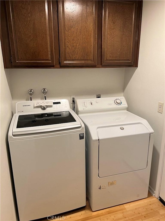 clothes washing area with cabinets, washer and dryer, and light wood-type flooring