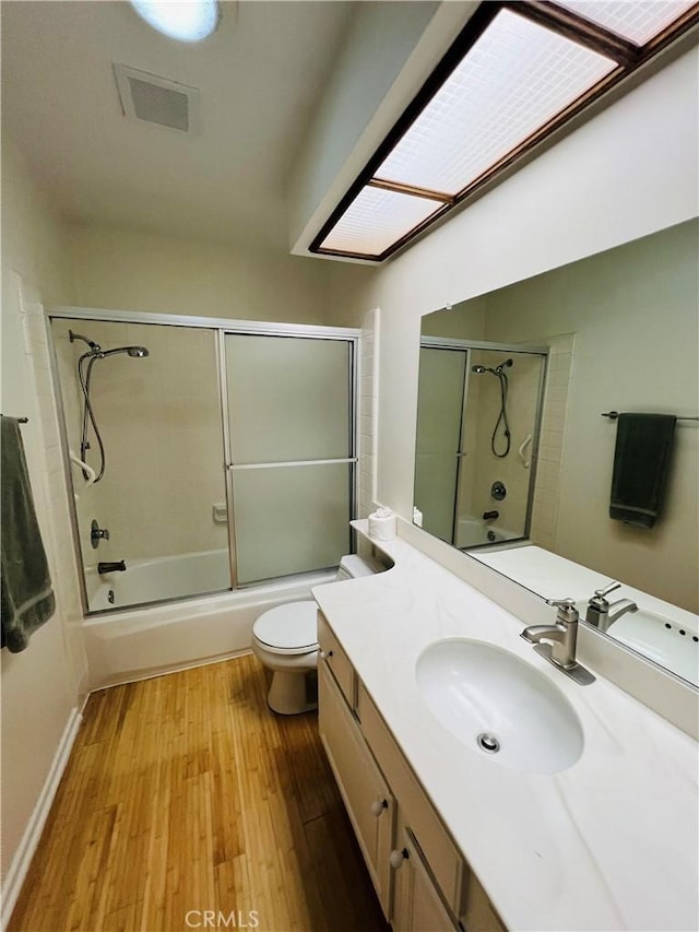 full bathroom featuring a skylight, wood-type flooring, enclosed tub / shower combo, vanity, and toilet