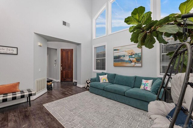 living room with a towering ceiling, plenty of natural light, and dark hardwood / wood-style floors