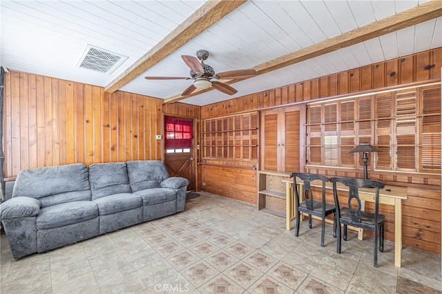 living room with ceiling fan, wooden walls, and beam ceiling