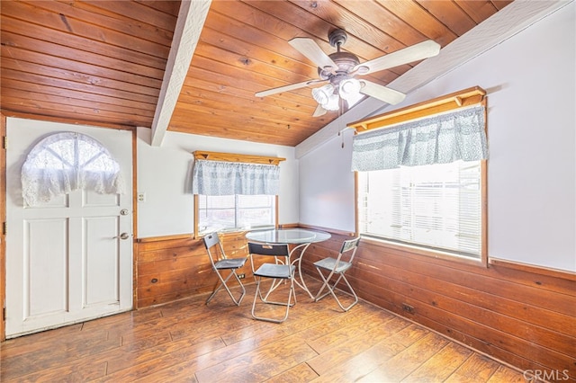 dining space with wood walls, vaulted ceiling with beams, hardwood / wood-style flooring, ceiling fan, and wooden ceiling