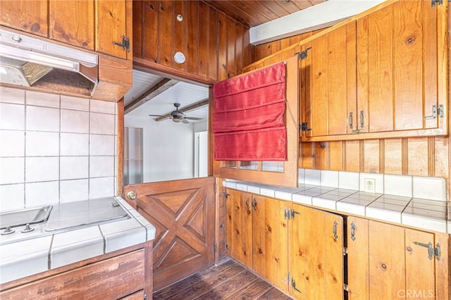 kitchen with beamed ceiling, dark wood-type flooring, wooden walls, and ceiling fan