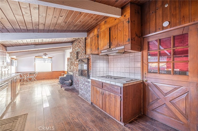 kitchen featuring stovetop, vaulted ceiling with beams, oven, dark hardwood / wood-style flooring, and tile counters