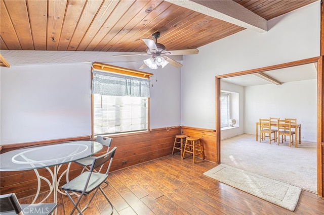 dining space with beamed ceiling, hardwood / wood-style flooring, a healthy amount of sunlight, and wooden walls