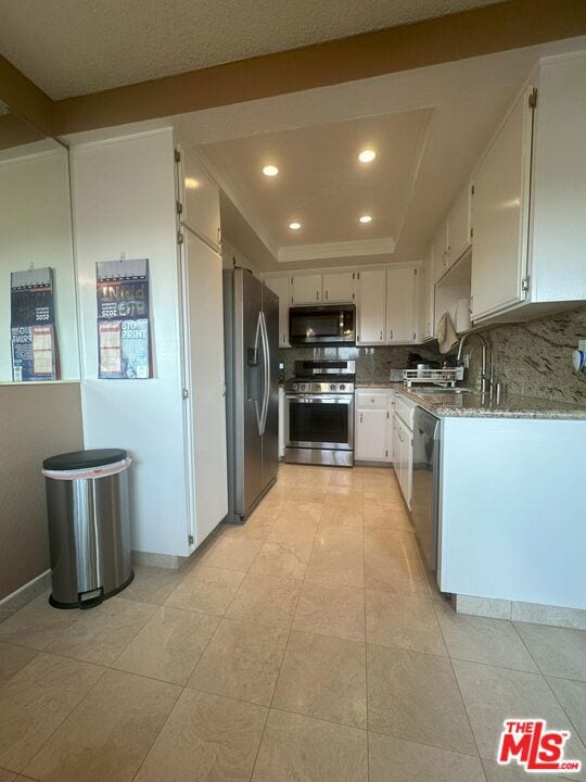 kitchen with sink, white cabinets, a tray ceiling, stainless steel appliances, and light stone countertops