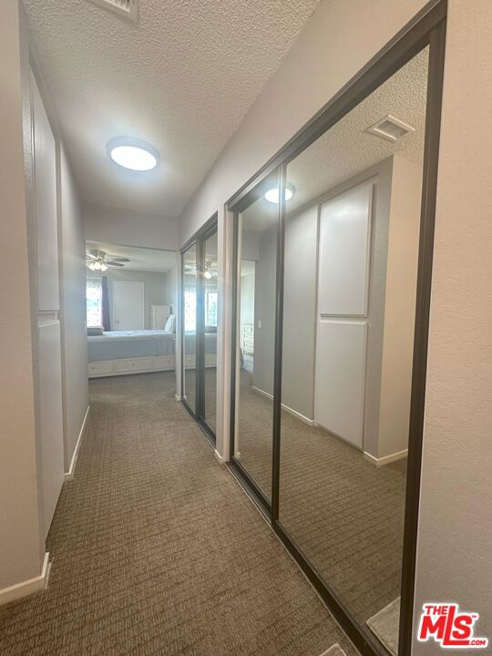 hall featuring a textured ceiling and dark colored carpet