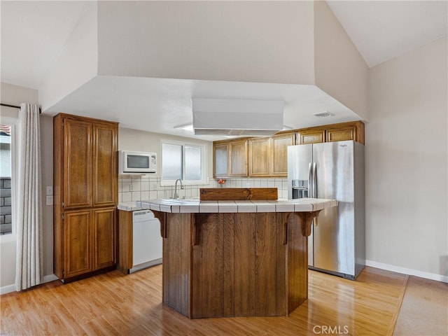 kitchen featuring tasteful backsplash, light wood-type flooring, tile counters, a kitchen breakfast bar, and white appliances