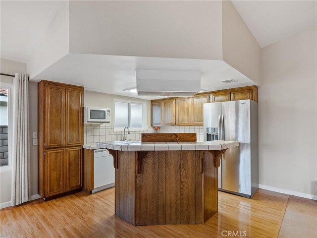 kitchen with tile countertops, light wood-type flooring, a kitchen breakfast bar, white appliances, and decorative backsplash