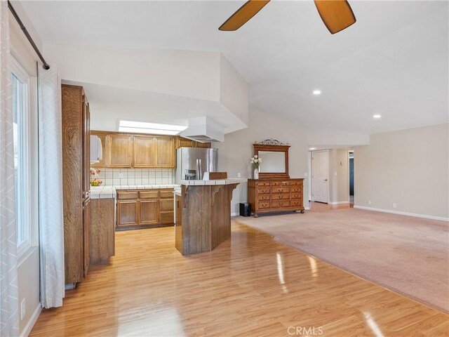 kitchen featuring a breakfast bar area, a center island, stainless steel fridge with ice dispenser, ceiling fan, and backsplash