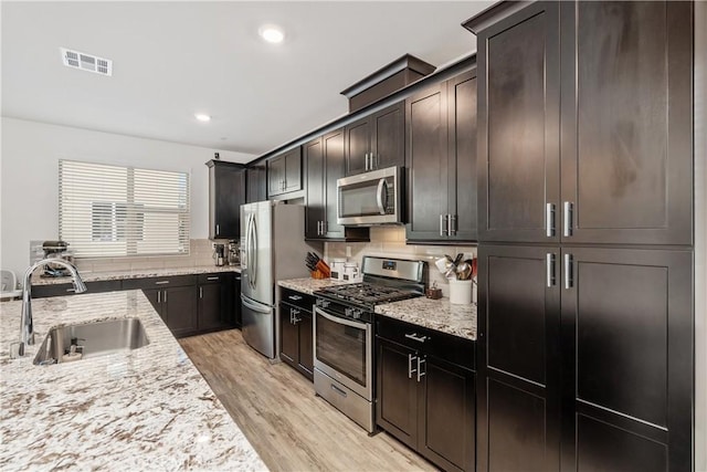 kitchen with sink, stainless steel appliances, light hardwood / wood-style floors, light stone countertops, and decorative backsplash