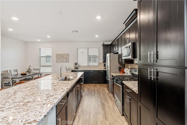 kitchen with sink, backsplash, stainless steel appliances, light hardwood / wood-style floors, and light stone countertops