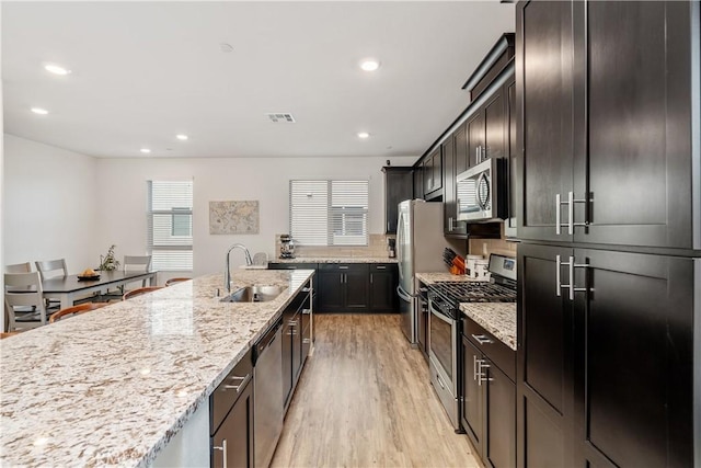 kitchen with sink, stainless steel appliances, light stone counters, tasteful backsplash, and light hardwood / wood-style floors