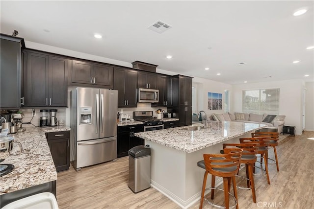 kitchen featuring sink, light hardwood / wood-style flooring, a kitchen island with sink, stainless steel appliances, and light stone countertops