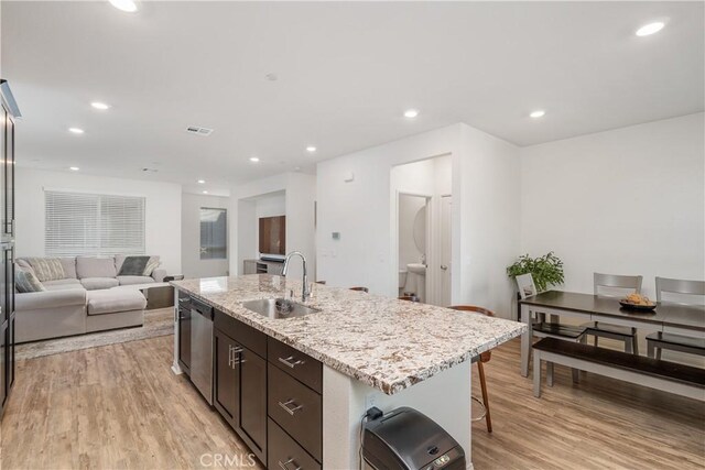 kitchen featuring sink, dark brown cabinets, light wood-type flooring, dishwasher, and an island with sink