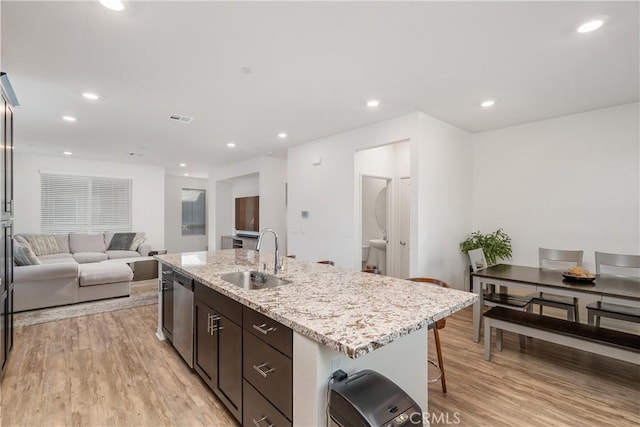 kitchen featuring sink, stainless steel dishwasher, dark brown cabinetry, light hardwood / wood-style floors, and a center island with sink