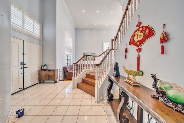 foyer entrance with crown molding, a towering ceiling, and light tile patterned floors