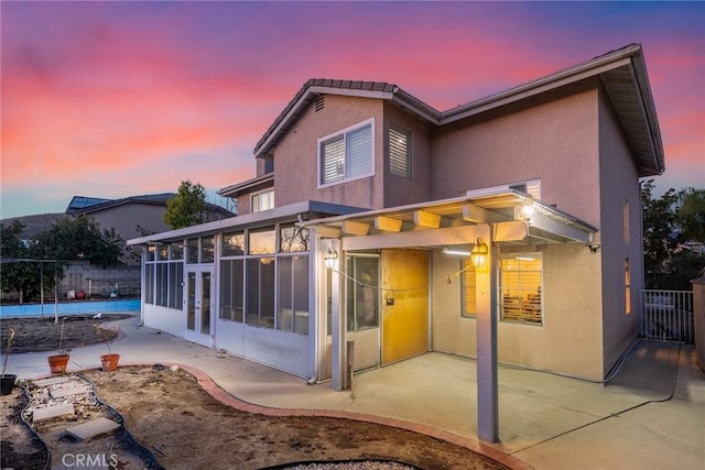 back house at dusk with a sunroom and a patio area