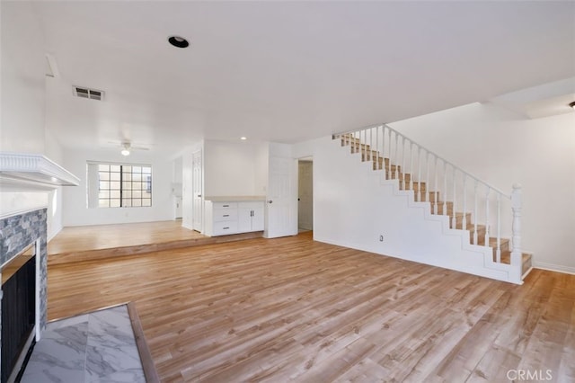 unfurnished living room with a fireplace, ceiling fan, and light wood-type flooring