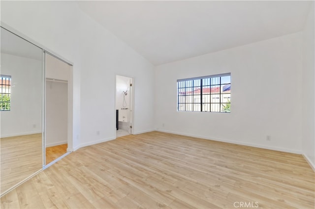 unfurnished bedroom featuring a closet, ensuite bathroom, high vaulted ceiling, and light hardwood / wood-style flooring