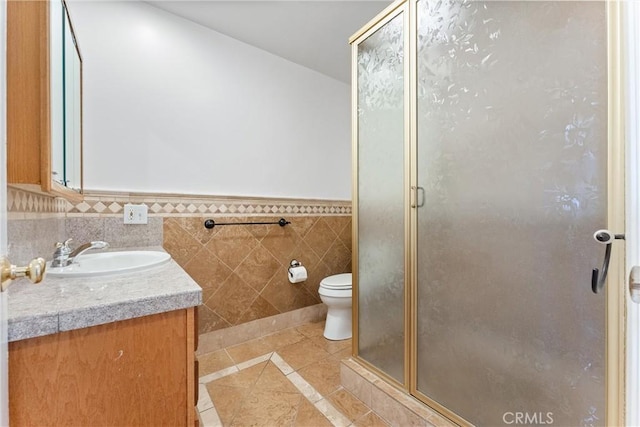 bathroom featuring tile patterned floors, toilet, an enclosed shower, tile walls, and vanity