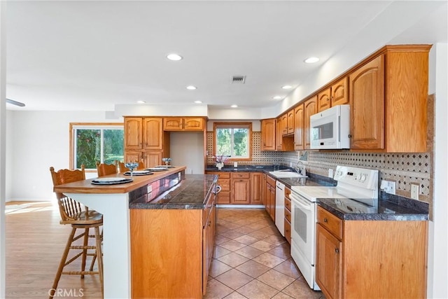 kitchen with sink, white appliances, backsplash, a center island, and a kitchen bar