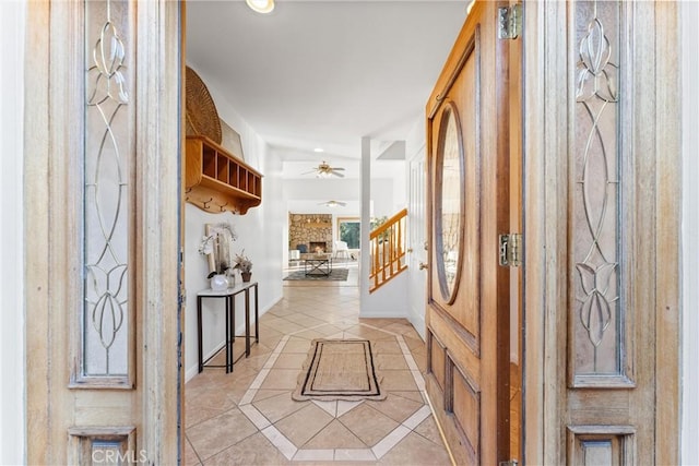 foyer with a stone fireplace, light tile patterned floors, and ceiling fan