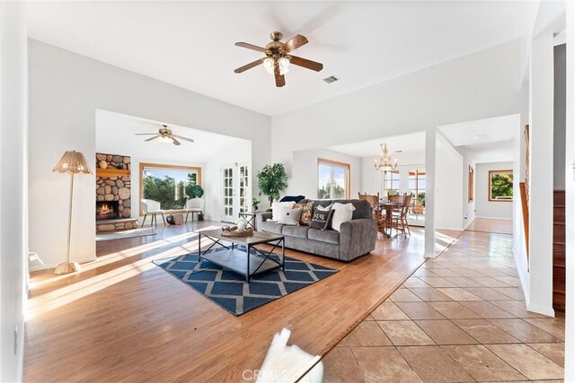 tiled living room with plenty of natural light, ceiling fan with notable chandelier, and a fireplace